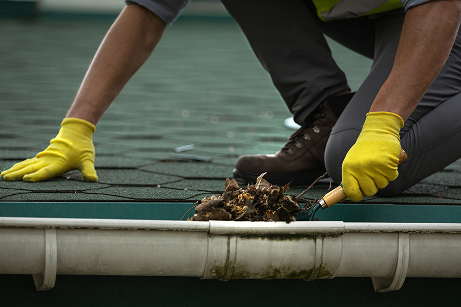 A man worker is cleaning a clogged roof gutter from dirt,